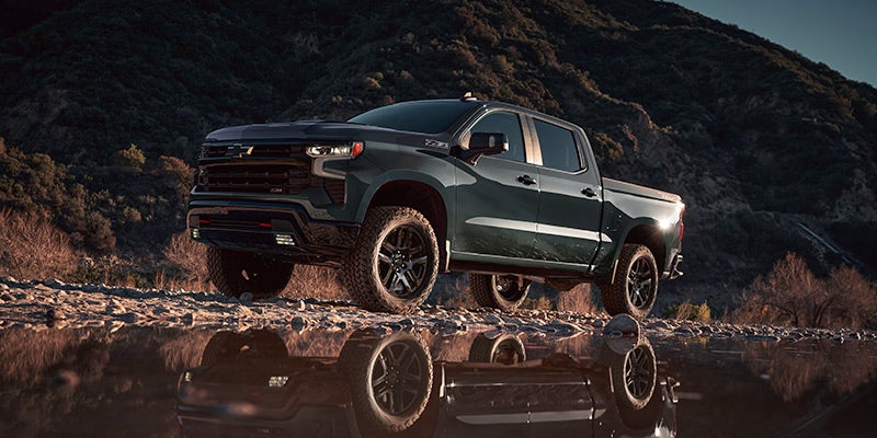 A dark green Silverado-1500 with a reflection in water.