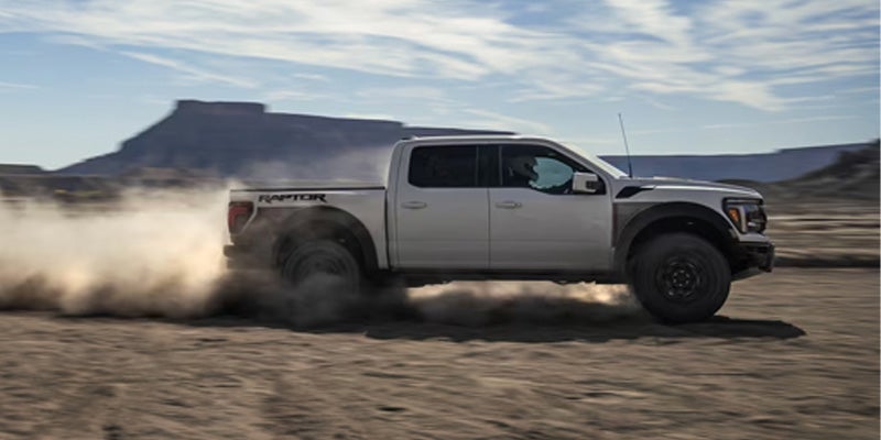 White Ford F-150 driving fast on desert terrain, dust trailing behind