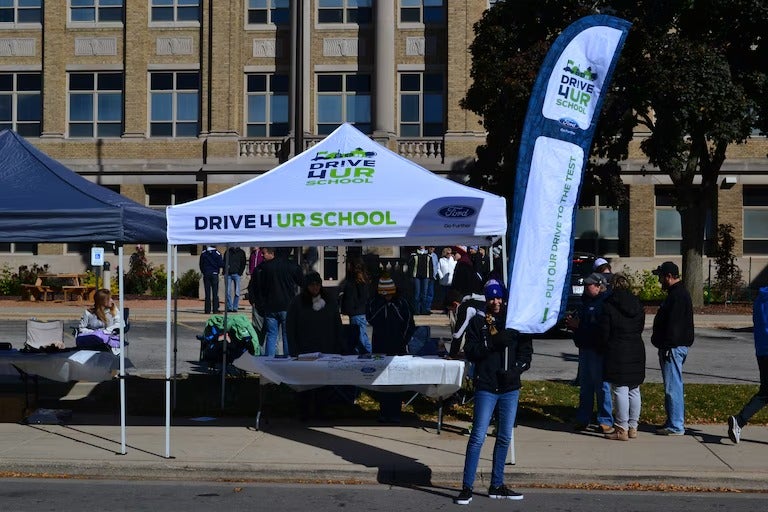 People gather under a Drive 4 UR School tent event