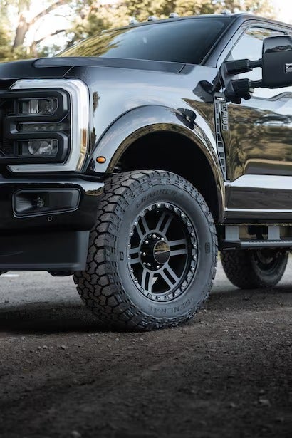A close-up of the front tire and black multi-spoke wheel of the truck.
