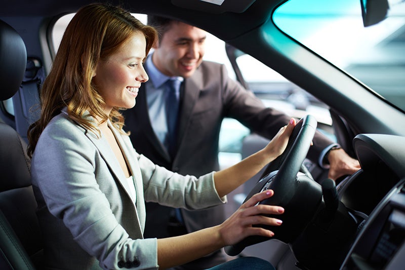 A happy women seating inside the car and a salesperson communicating with her